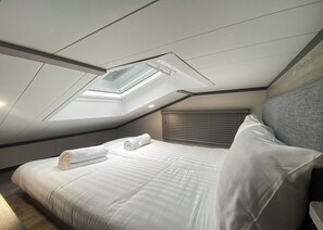 Une chambre avec un puits de lumière, un lit avec du linge de lit blanc et une tête de lit.