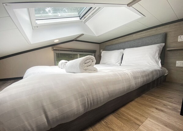 Una camera da letto con un lucernario, un letto con biancheria bianca e un pavimento in legno.