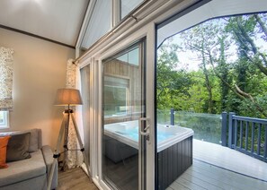 A room with a sliding glass door leading to an outdoor deck, a sofa, a floor lamp, and a hot tub.