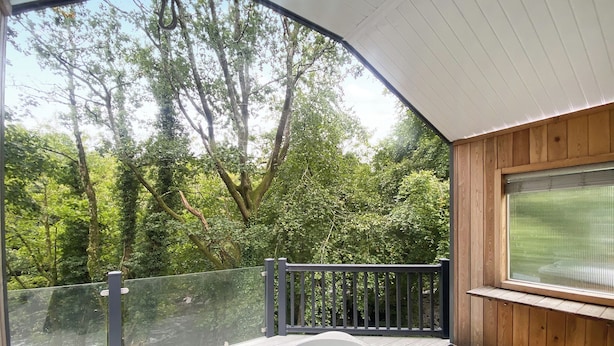 A hot tub on a wooden deck with a view of a forest. - Relax and unwind in the perfect hideout. (Snowdonia)