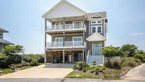 A multi-story residential building with a balcony on the second floor, a garage entrance, and a well-maintained front yard. - Shiner Shore Shack: 1200 Ft to Beach Access, Pool, Hot Tub (Corolla)