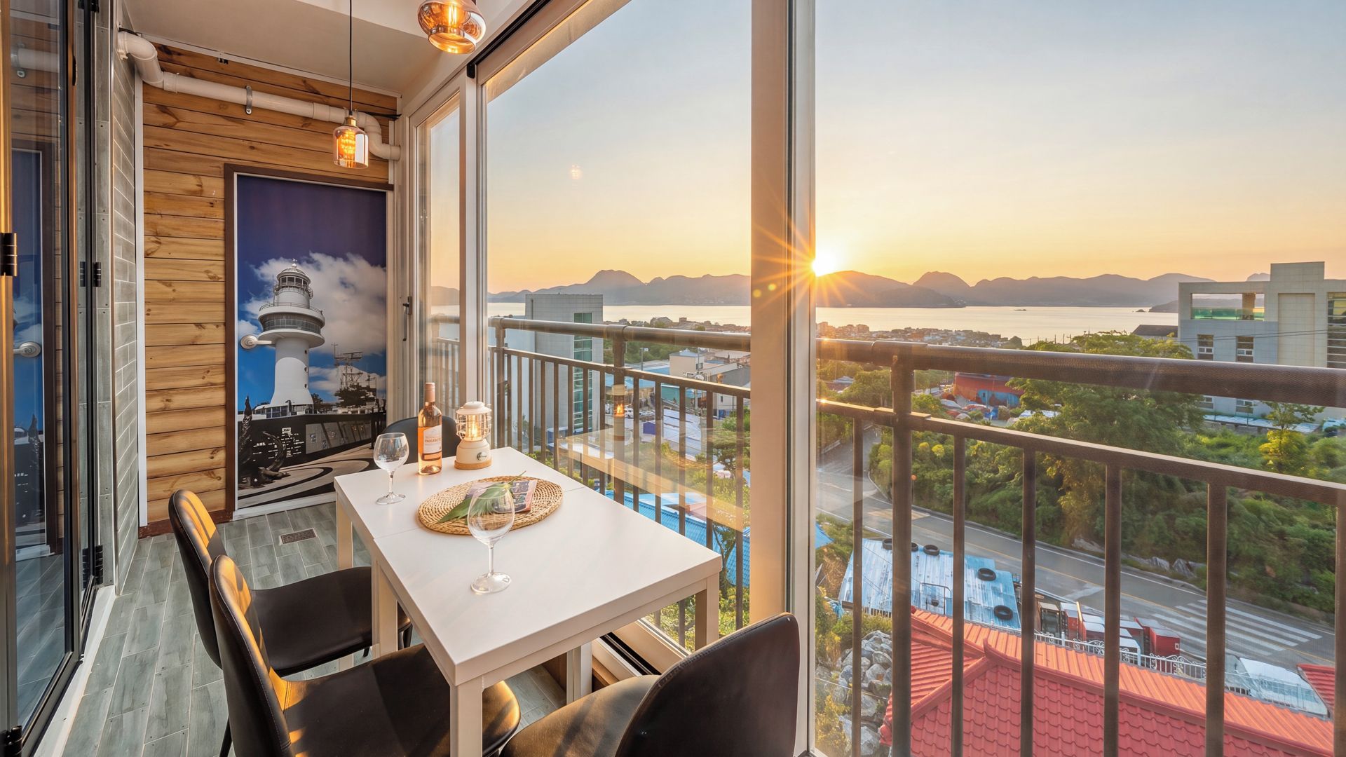 A balcony with a table set for dining, a view of the sea, and a lighthouse mural on the wall.
