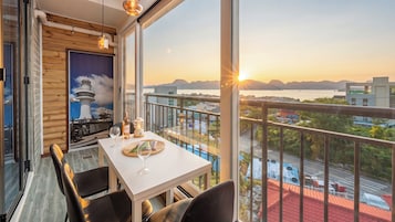 A balcony with a table set for dining, a view of the sea, and a lighthouse mural on the wall.