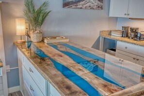 A kitchen with a wooden countertop, a blue water feature, a plant, and a coffee maker.
