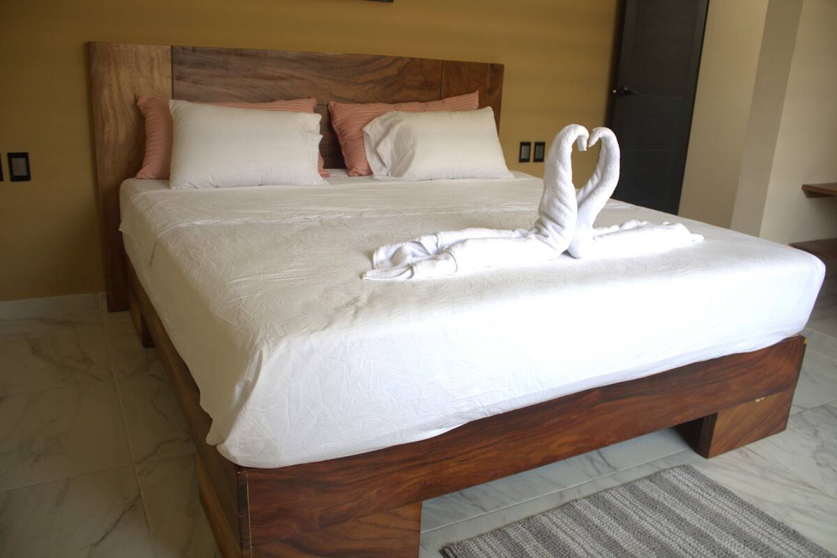 A neatly made bed with a heart-shaped towel arrangement, a wooden headboard, and a marble-tiled floor.