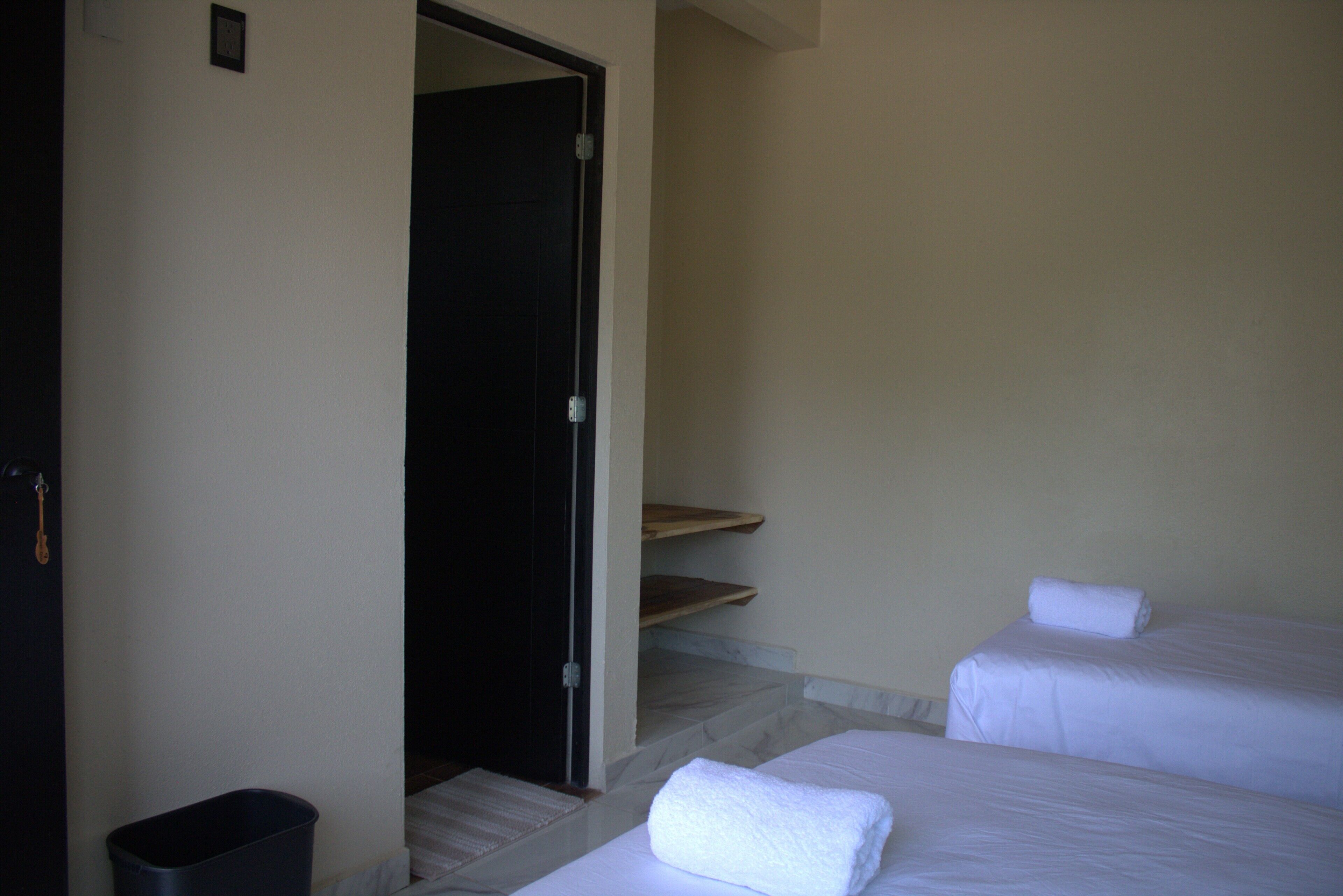 Ein Hotelzimmer mit zwei Betten, einer kleinen Mülltonne und einer Tür zu einer Treppe.