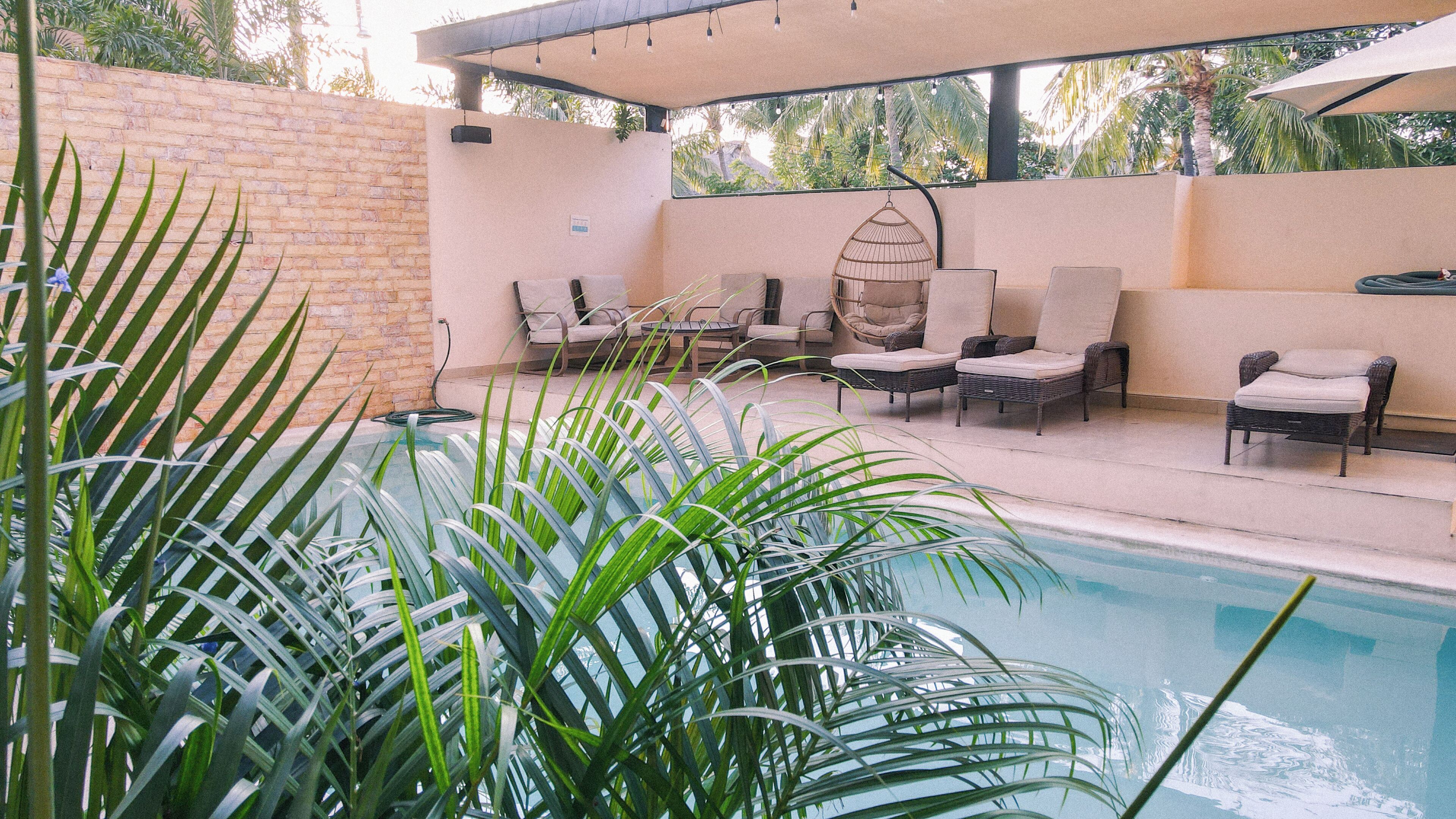 A poolside area with lounge chairs, a hanging light fixture, and a brick wall.