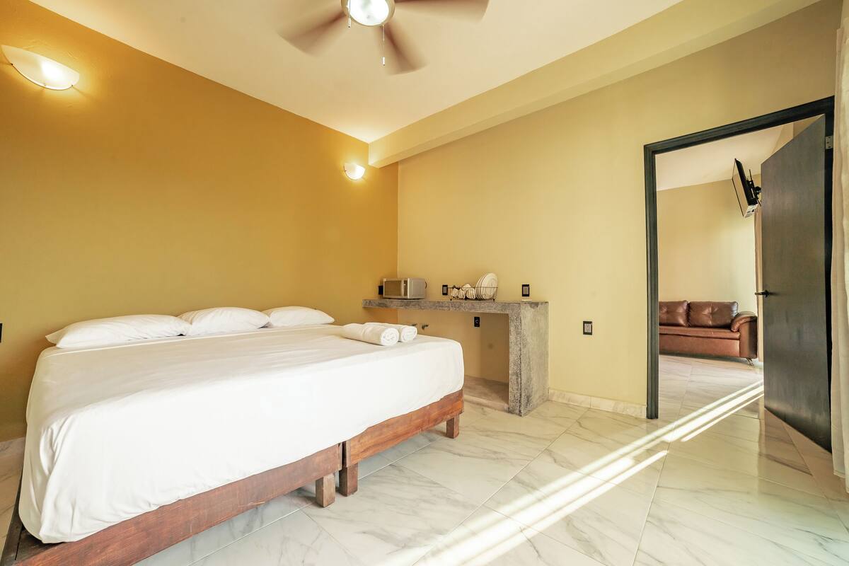 A bedroom with a bed, a ceiling fan, a nightstand, and a door leading to another room.