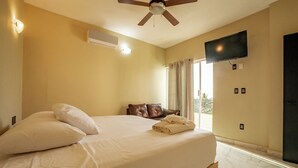 A hotel room with a bed, a ceiling fan, a flat-screen TV mounted on the wall, and a window with curtains. - Hotel Guitarra Inn (Puerto Escondido)
