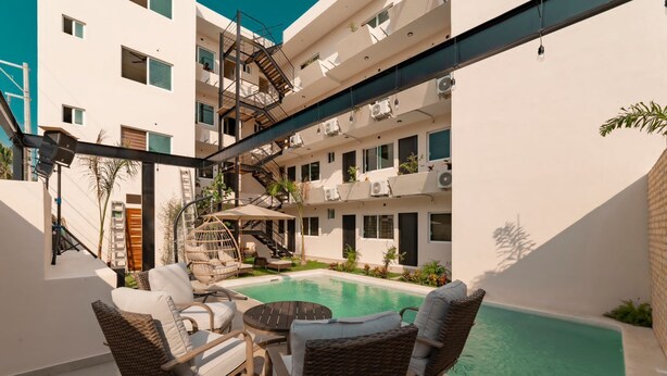 A modern outdoor pool area with wicker furniture and a staircase leading to an upper level. - Hotel Guitarra Inn (Puerto Escondido)