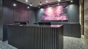 A modern reception desk with a laptop, overhead lighting, and a large abstract painting on the wall.