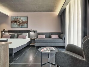 A modern hotel room with a bed, sofa, armchair, bedside table, and a small round table with magazines. - Number 11 St Julian's Malta-handwritten Collection (St. Julian's)