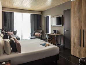 Une chambre d’hôtel moderne équipée d’un lit, d’un bureau, d’une chaise, d’une télévision et d’une armoire.