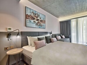 A modern hotel room with a large bed, a bedside table, a wall-mounted lamp, a painting, and a view of the outdoors. - Number 11 St Julian's Malta-handwritten Collection (St. Julian's)