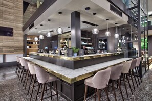A modern bar area with a marble countertop, bar stools, and pendant lighting.