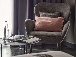 A modern armchair with a cushion, a glass bottle, two glasses, and a magazine on a small table. - Number 11 St Julian's Malta-handwritten Collection (St. Julian's)