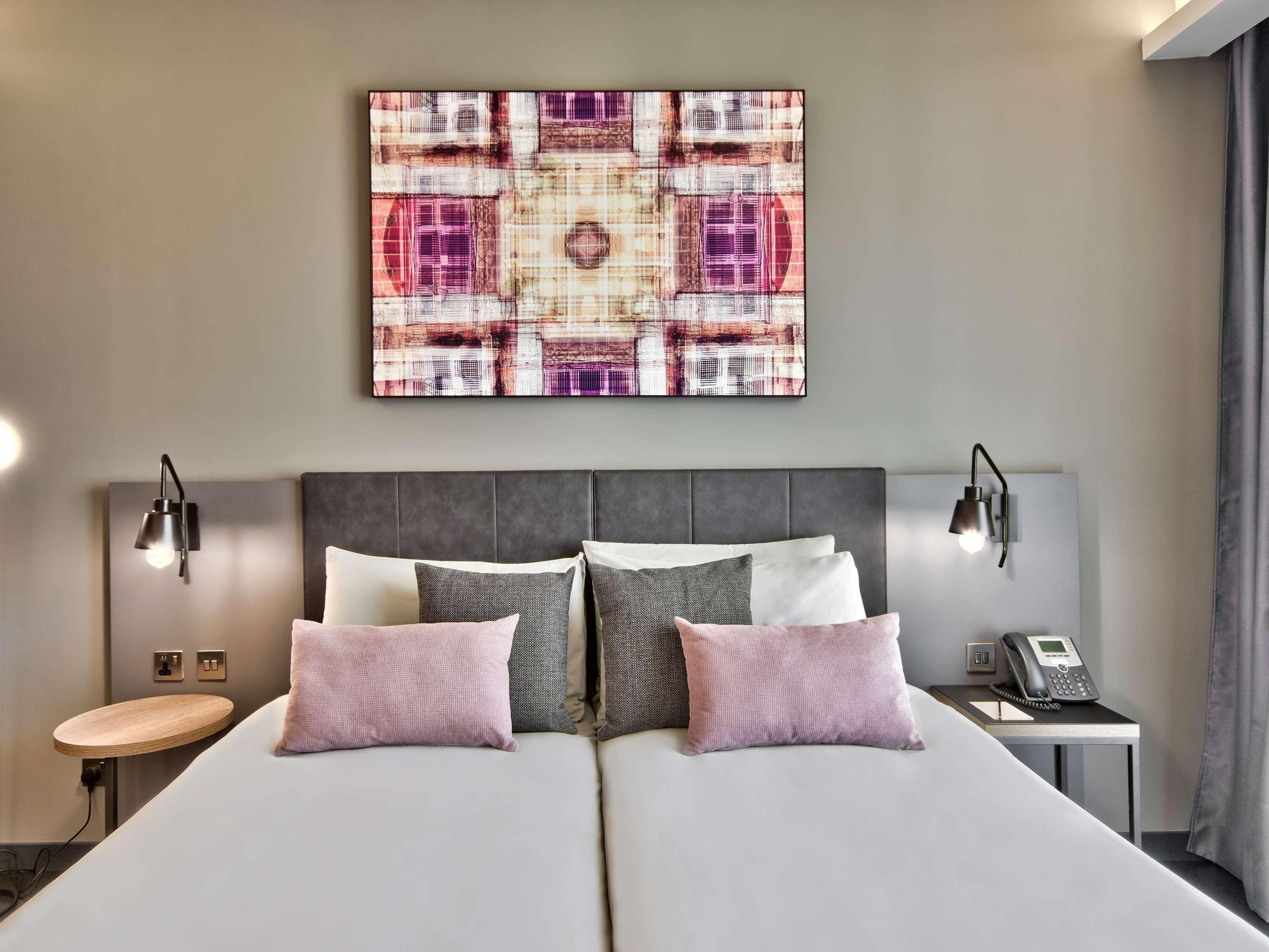 Une chambre d’hôtel avec un grand lit, deux lampes de chevet, un téléphone sur la table de chevet et une œuvre d’art accrochée au mur.