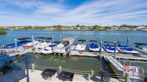 Un port de plaisance avec des bateaux amarrés à des quais en bois, un panneau indiquant les services proposés et une vue dégagée sur l’eau et la côte lointaine.