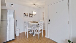 Een compacte, schone keuken met een roestvrijstalen koelkast, een witte eettafel met vier stoelen en een hanglamp.
