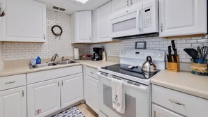 A kitchen with white cabinets, a microwave, a stove, and a sink. - Caddy's #5 – Waterfront Balcony, Walk to Beach, Pet-Friendly & Next to Dining (Indian Shores)