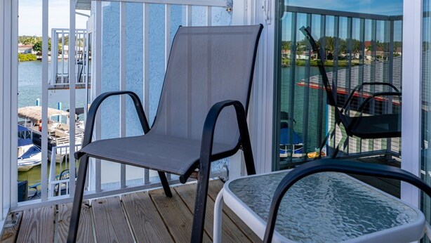 A balcony with a chair and a table, overlooking a body of water with boats and a marina.