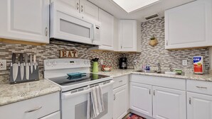 A kitchen with white cabinets, a microwave, an oven, and a sink. There is a 'EAT' sign on the wall and a colorful rug on the floor.