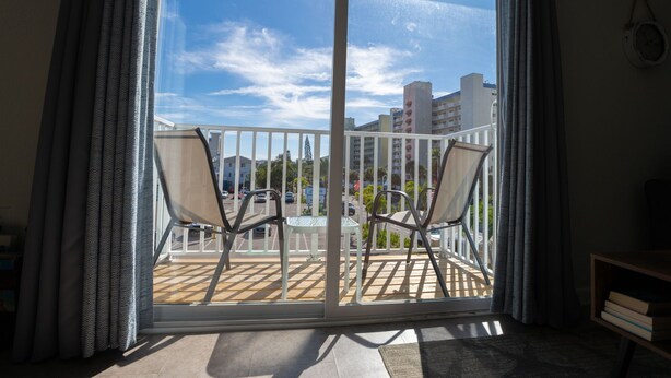 A balcony with two chairs and a table, overlooking a cityscape with buildings and a clear sky. - Caddy's #8 – Walk to Beach, Pet-Friendly, Full Kitchen & Steps to Dining (Indian Shores)
