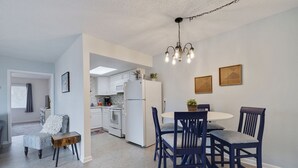 A modern kitchen with white appliances, a dining area with dark blue chairs, and a chandelier. - Caddy's #8 – Walk to Beach, Pet-Friendly, Full Kitchen & Steps to Dining (Indian Shores)