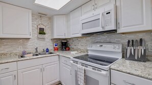 A modern kitchen with white cabinets, a built-in microwave, an electric stove, and a knife block. - Caddy's #8 – Walk to Beach, Pet-Friendly, Full Kitchen & Steps to Dining (Indian Shores)