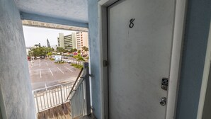 A view from a balcony to a parking lot with a building in the background. - Caddy's #8 – Walk to Beach, Pet-Friendly, Full Kitchen & Steps to Dining (Indian Shores)