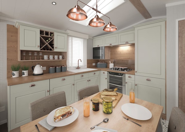 A modern kitchen with light green cabinets, a wooden countertop, a built-in stove, and a dining area with a table set for a meal.