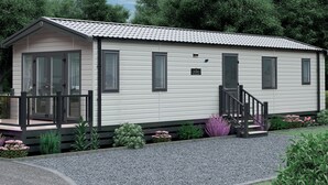 En etagers mobilhome med en veranda, en lille terrasse og en grusvej.