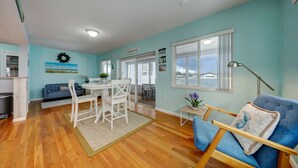Un vaste espace de vie comprenant une table à manger, des chaises, un canapé bleu et une vue sur l’extérieur grâce  à de grandes fenêtres.