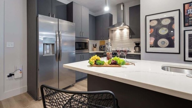 A modern kitchen with a large island, stainless steel appliances, and a hanging light fixture. - Tria - 2 Condos - Odyssey (Nashville)