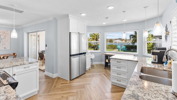 Una cocina moderna con armarios blancos, electrodomésticos de acero inoxidable, una encimera de granito y vistas a una piscina y palmeras.
