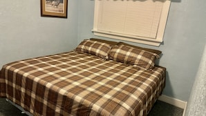 Een slaapkamer met een geruite sprei, een ingelijst foto aan de muur en een raam met jaloezieën.
