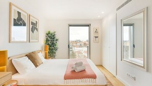 A modern bedroom with a large bed, a bedside lamp, a mirror, and framed artwork on the wall. - GuestReady - Central Park in Porto (Porto)