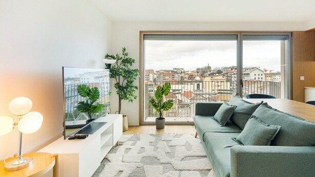A modern living room with a large window, a sofa, a TV, and a potted plant. - GuestReady - Central Park in Porto (Porto)