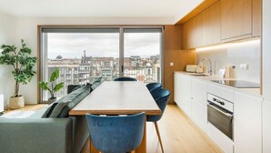 A modern apartment with a dining area, kitchen, and large windows offering a city view. - GuestReady - Central Park in Porto (Porto)