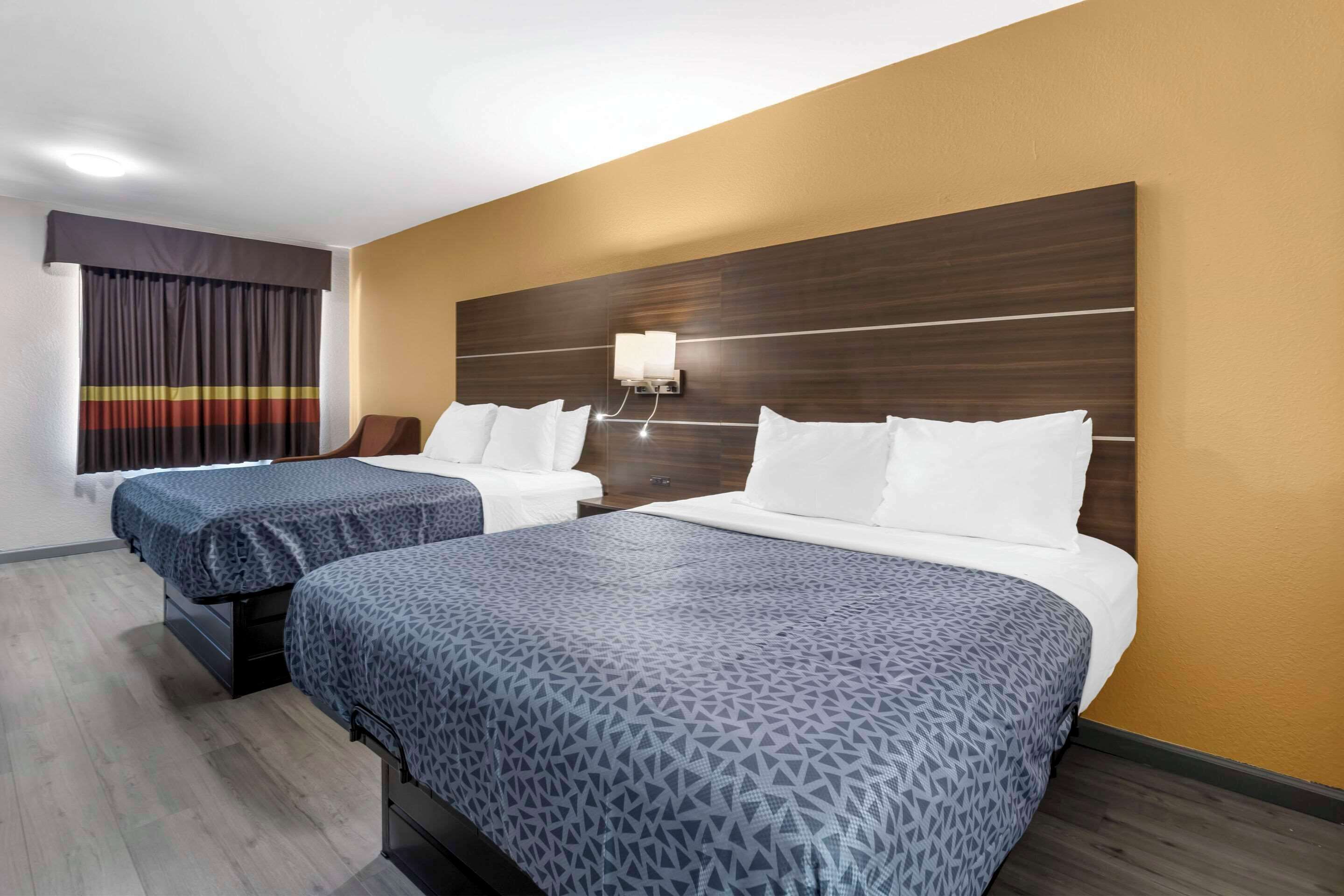 A hotel room with two beds, a wooden headboard, a nightstand, and a window with curtains.