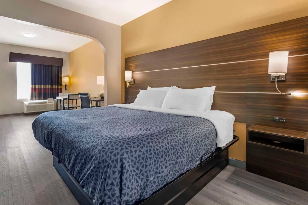 A hotel room with a bed, bedside tables, a desk with a chair, and a window with curtains.