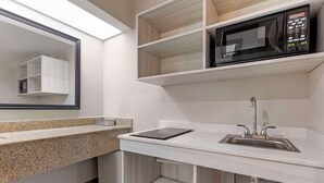 A modern kitchen with a granite countertop, a built-in microwave, a sink, and a mirror above the counter. - Suburban Studios Orangeburg (Orangeburg)