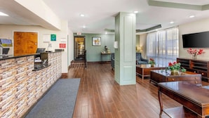 A reception area with a stone wall, wooden reception desk, and a seating area with a TV and plants. - Suburban Studios Orangeburg (Orangeburg)