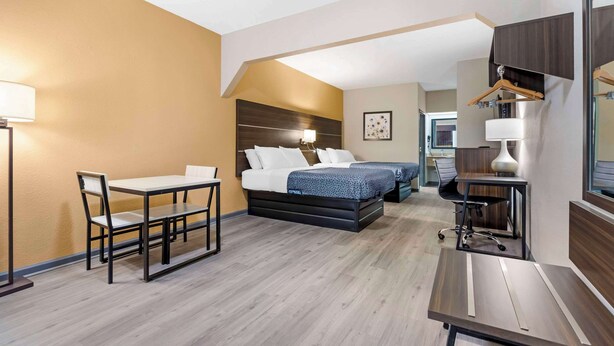 A hotel room with a bed, a desk, a chair, and a hanging coat rack. - Suburban Studios Orangeburg (Orangeburg)