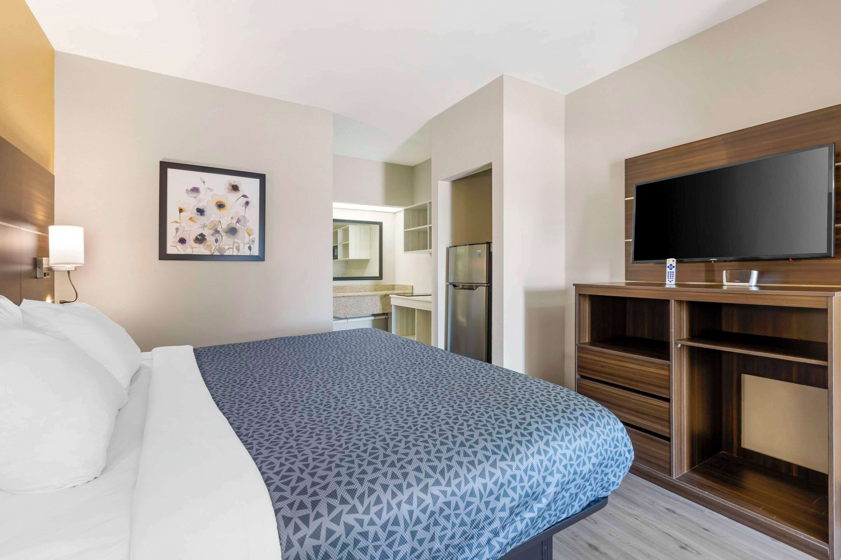 Ein Hotelzimmer mit Bett, Fernseher, Kühlschrank und einem durchgegangenen Tür sichtbaren Badezimmer.