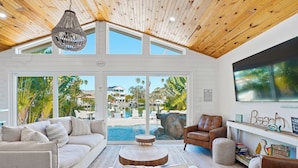 Un salon spacieux doté d’une grande fenêtre donnant sur une piscine et un paysage tropical.