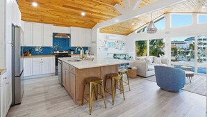 Une cuisine moderne avec un plafond en bois, des armoires blanches et un îlot central doté de tabourets.