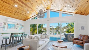 Un vaste espace de vie doté d’un plafond en bois, offrant une vue sur la piscine, comprenant une table à manger et un coin salon confortable.