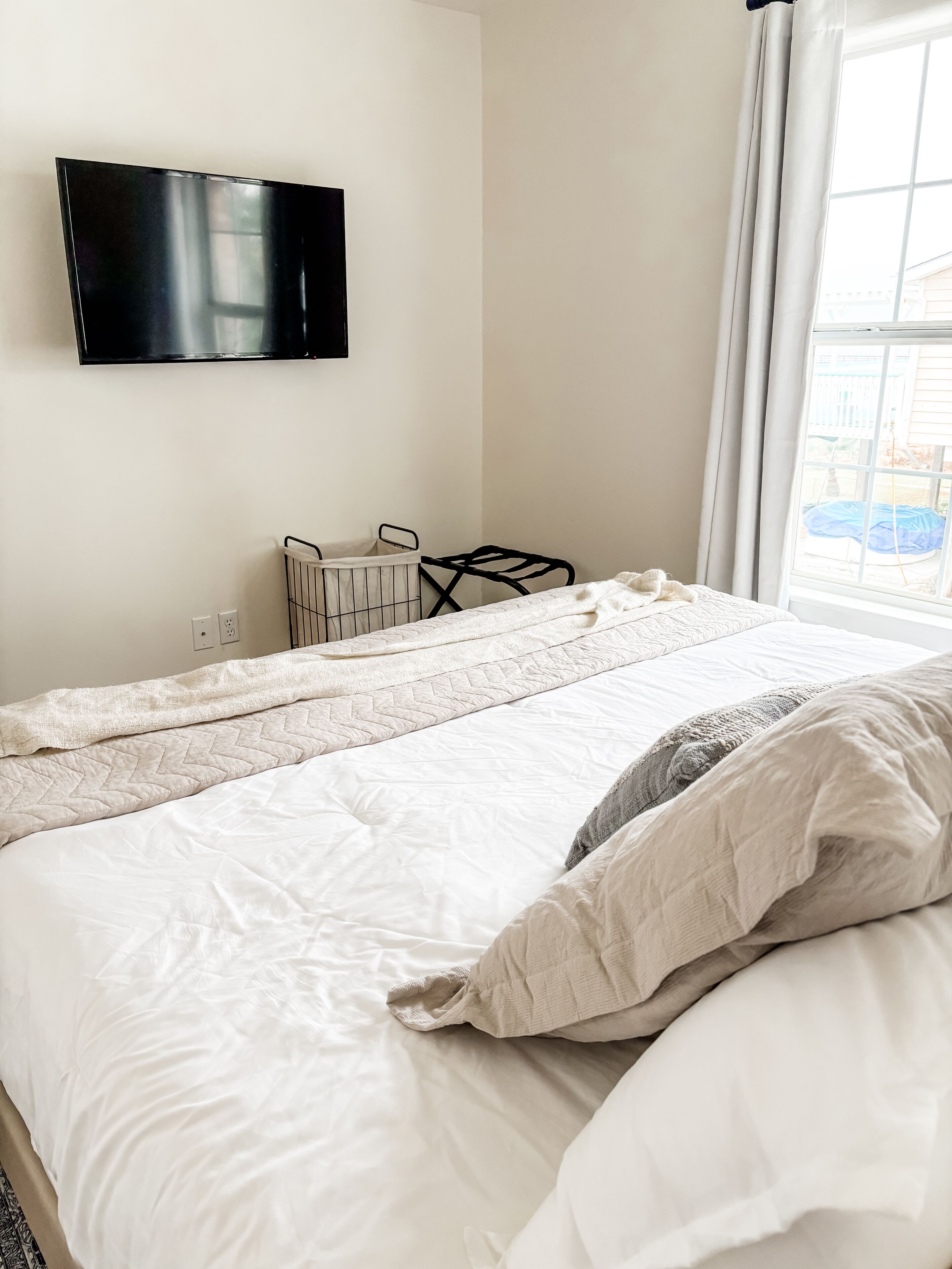 A hotel room with a bed, a TV mounted on the wall, a window with curtains, and a radiator.