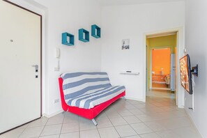 A room with a sofa, a door, a wall-mounted phone, and a TV.